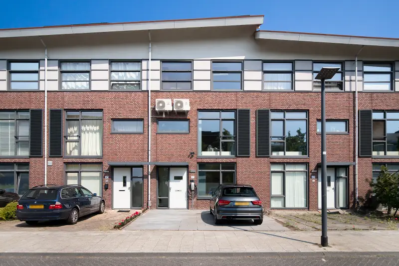 Vooraanzicht van de tussenwoning met bakstenen gevel, dubbele oprit en laadpaal