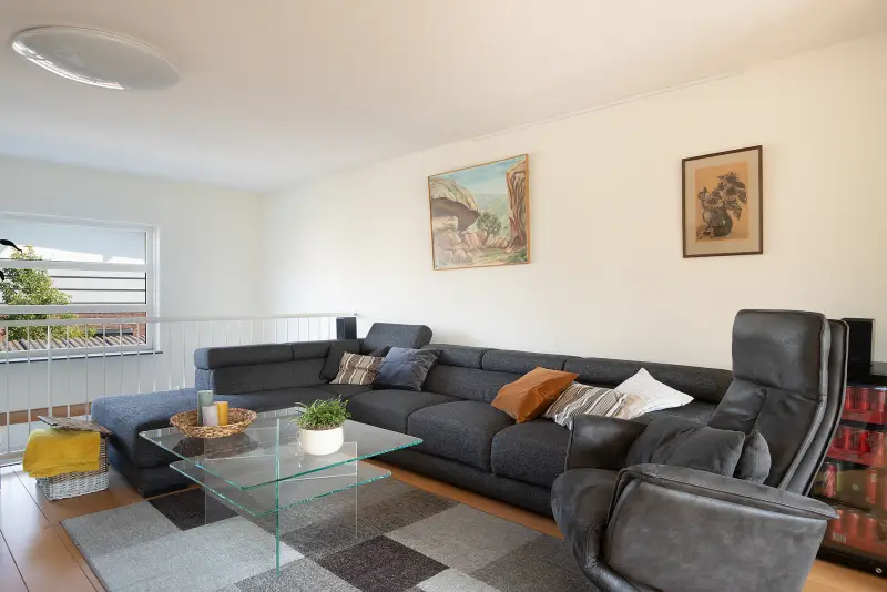 Zithoek in de woonkamer met bank, salontafel en balustrade langs de vide