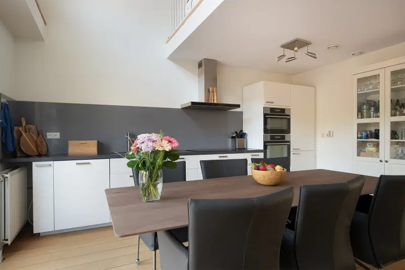 Keuken met lichte kasten, grijze achterwand, inbouwapparatuur en eettafel