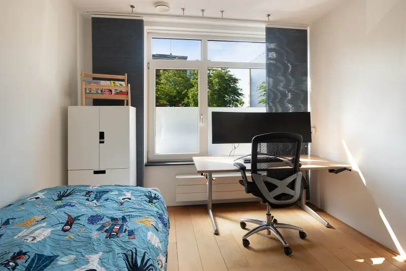 Werk- en slaapkamer met bureau bij het raam en eenpersoonsbed