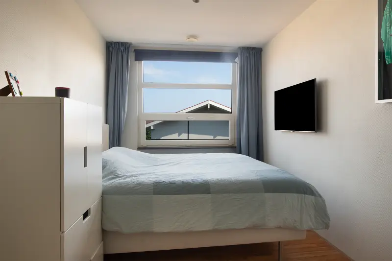 Slaapkamer met tweepersoonsbed, kastruimte en uitzicht over de wijk