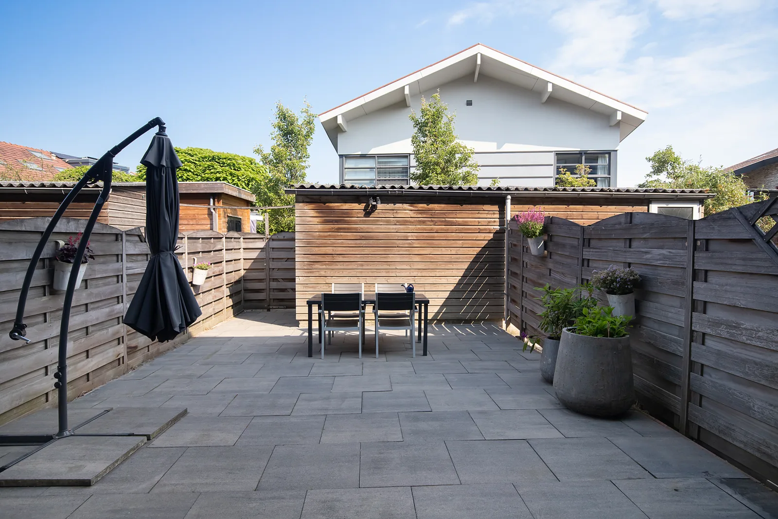 Onderhoudsarme achtertuin op het noordwesten met bestrating, eethoek en houten schutting voor privacy