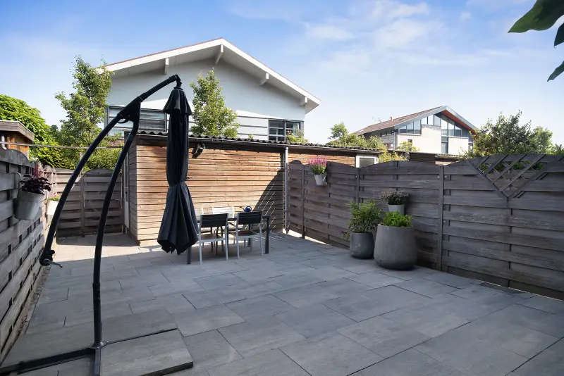 Achtertuin met bestrating, eethoek, parasol en houten berging