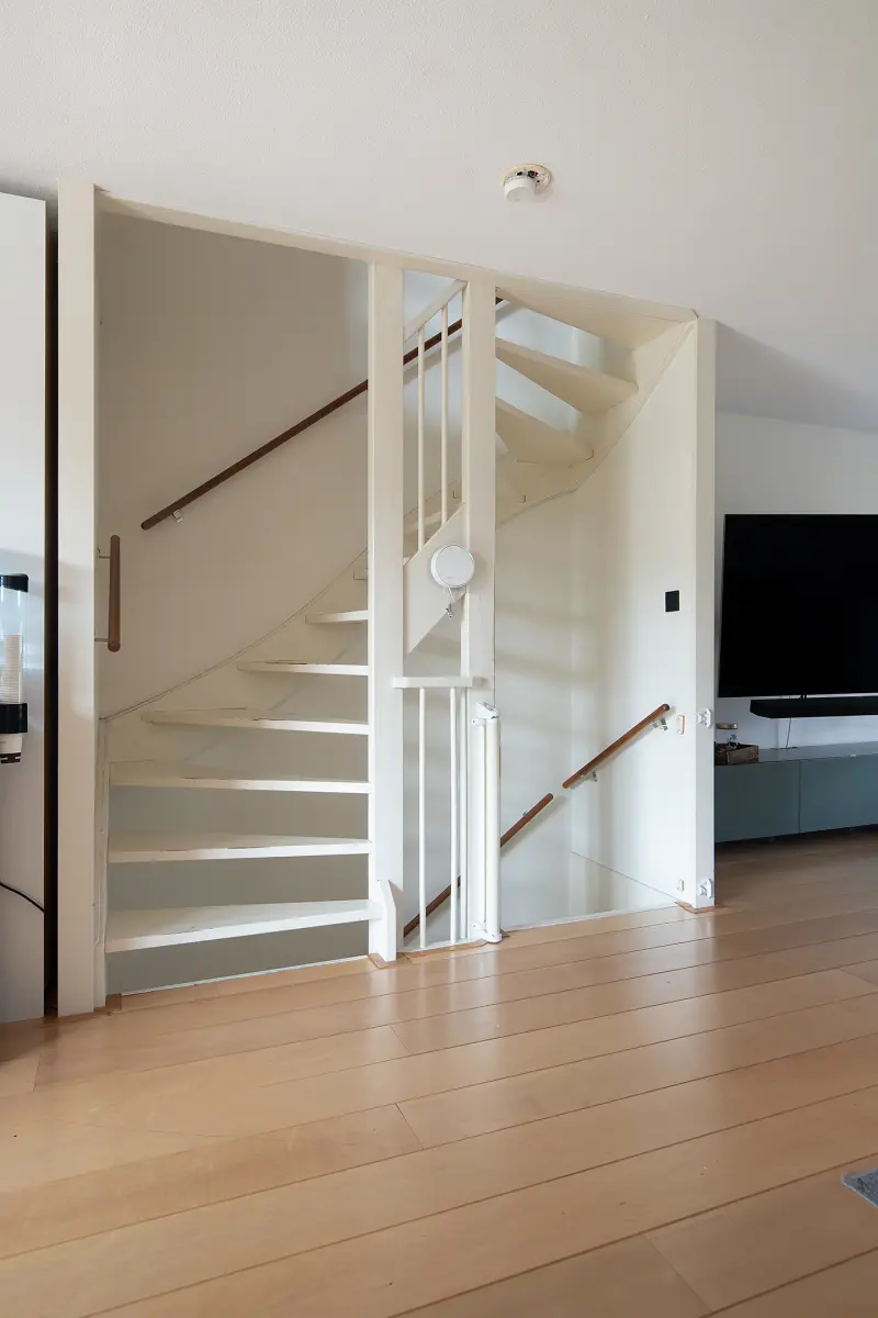 Open witte houten trap met houten leuning die de woonlagen verbindt